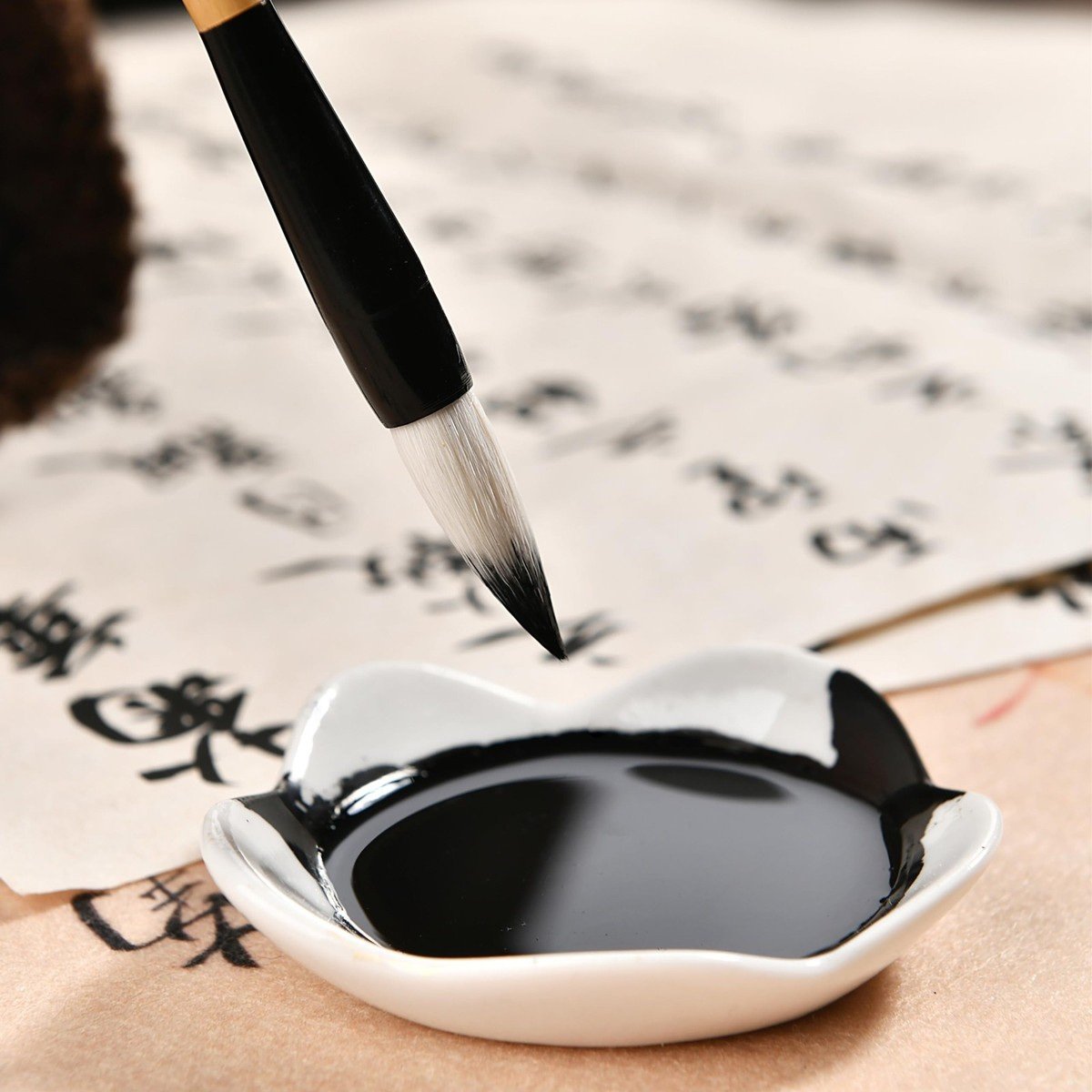 A calligraphy brush dipping into black ink, with written characters beyond.